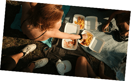 Friends sharing takeout fries and wraps on a picnic blanket