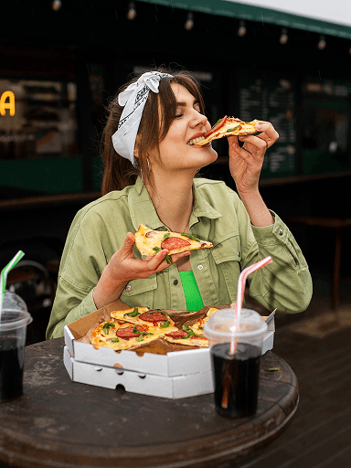 A woman enjoying a slice of pizza outside a street food truck
